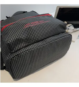 Detail of checkered canvas backpack with red zippers near laptop and headphones