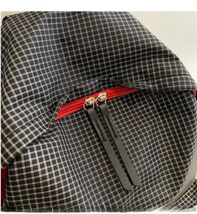 Macro detail of smooth red zipper with long leather pullers on black and white plaid backpack