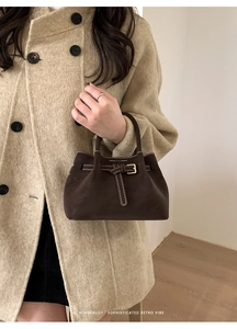 Macro shot of a dark brown suede bucket bag with white contrast stitching and metal buckle