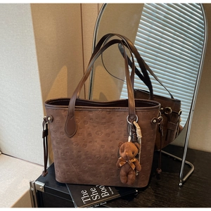 Close-up of brown tote bag with dog embossing, drawstring detail, and plush bear charm