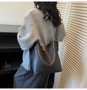 Detail of black leather bucket bag featuring a square gold buckle and adjustable strap