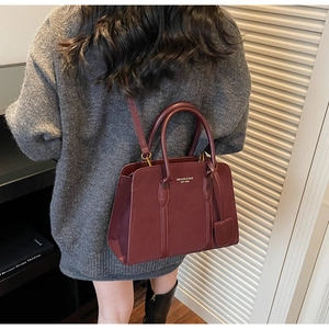 Model trägt eine burgunderrote Ledertragetasche mit Goldlogo und abnehmbarem Schultergurt
