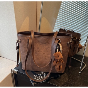 Detail of coffee brown tote bag featuring embossed dog pattern and plush bear charm