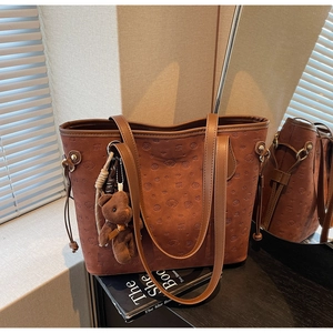 Detail shot of brown embossed leather tote bag with teddy bear charm on book background