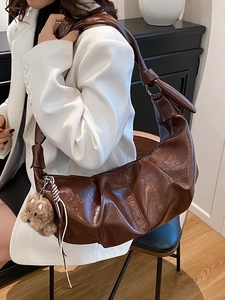 Brown ruched crescent shoulder bag in glossy faux leather with a cute bear charm accessory
