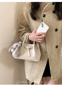 Detail of cream leather bucket bag with plush bunny charm and elegant metal clasp buckle