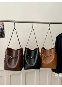 Trois sacs seaux en marron foncé, noir et beige suspendus à un support métallique