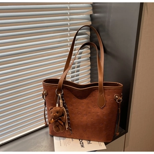 Detail of embossed brown tote bag with plush bear charm and striped scarf decoration