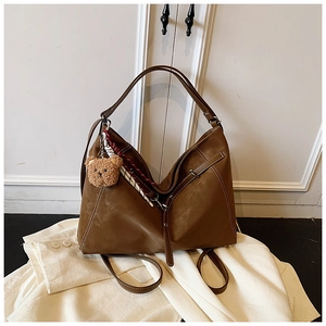 Detail of vintage brown tote bag with white stitching, plush bear charm, and plaid scarf