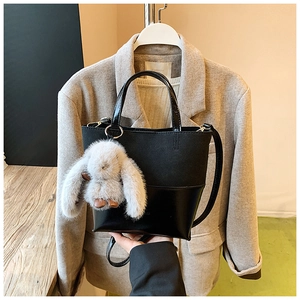 Detail of black PU leather tote bag with a fluffy grey plush rabbit keychain accessory