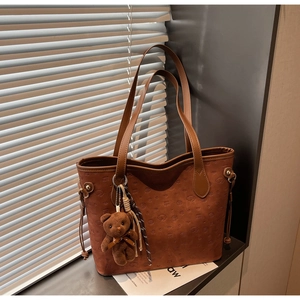 Detail of dark brown tote bag featuring embossed puppy patterns and a cute bear charm