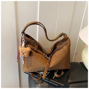Close-up of brown suede tote bag featuring white contrast stitching and a plush bear charm