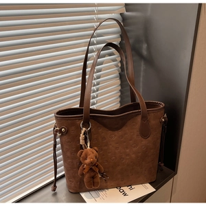 Close-up of brown tote bag with embossed dog pattern, Ni Baw logo and plush bear charm
