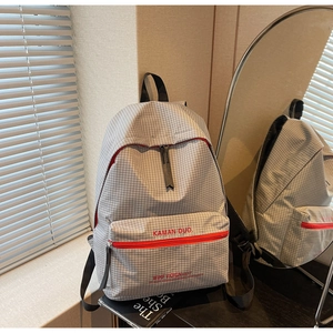 Close-up of grey plaid backpack featuring red zipper details and printed text graphics