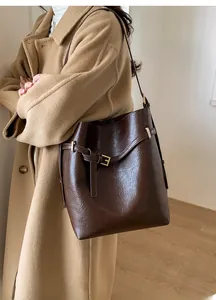 Détail d'un sac seau en cuir marron foncé avec boucle décorative porté par un mannequin