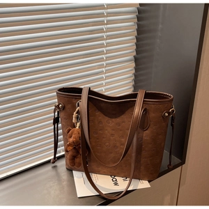 Detail of dark brown tote bag with embossed cartoon dog patterns and plush bear charm