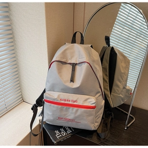 Detail of grey plaid backpack with red zipper and KAMAN DUO text on front pocket