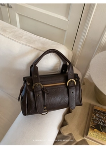 Gros plan d'un sac Boston rétro marron avec boucles dorées sur un canapé beige
