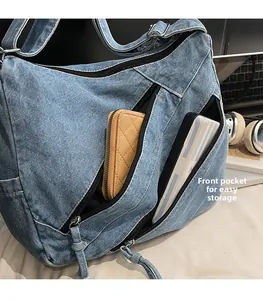 Detail view of front zipper pocket on denim shoulder bag storing wallet and power bank