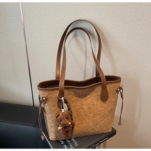 Detail of brown tote bag with embossed cartoon dog patterns and plush bear charm accessory