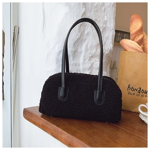 Détail d'un sac cabas en peau de mouton noire avec anses en cuir sur une table