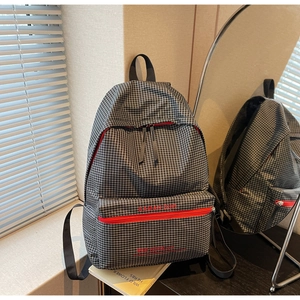 Detail view of plaid backpack featuring contrasting red zippers and premium fabric texture