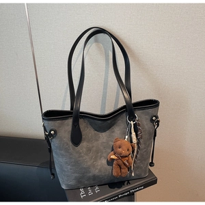 Detail view of a gray embossed dog tote bag with a brown teddy bear plush charm