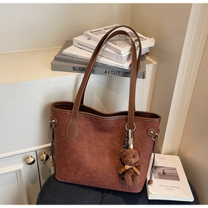 Detail of a dark brown suede tote bag with embossed bear and heart patterns and plush charm