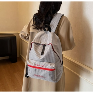 Close-up of minimalist grey plaid backpack with a red zipper front pocket detail