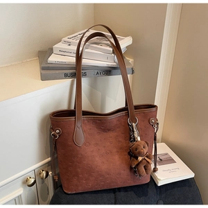 Detail of brown tote bag with embossed cartoon patterns and plush bear charm decoration