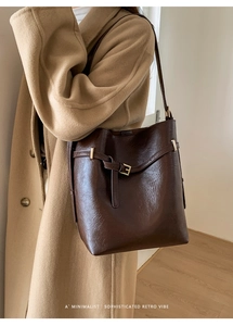 Détail du sac seau en cuir marron foncé avec boucle dorée et sangle sur le mannequin