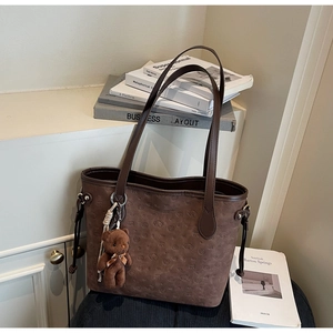 Detail of dark brown tote bag with embossed patterns and a plush bear pendant