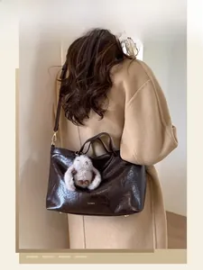 Detail of dark brown wax leather tote with gold logo and plush rabbit pendant decor