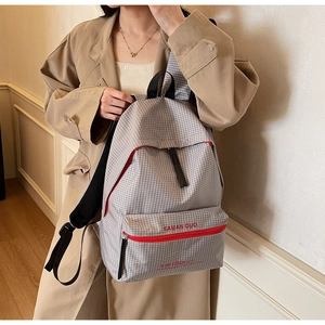Detail of grey plaid canvas backpack featuring vibrant red zippers and brand lettering