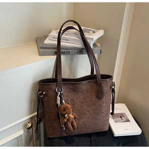 Detail of dark brown tote bag featuring embossed patterns and a plush bear pendant