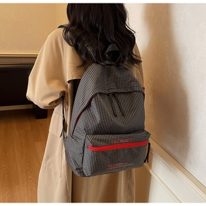 Detail of checkered canvas backpack showing red zipper pocket and embroidered logo