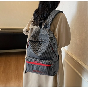 Detail of checkered backpack with red zipper and logo shown on person in beige coat