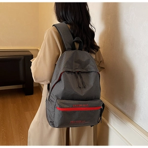 Detail view of stylish black and white plaid backpack with red accent on a model's back