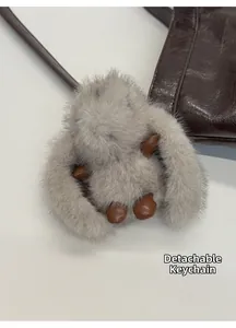Detail of a gray plush rabbit charm with leather feet on a brown leather shoulder bag