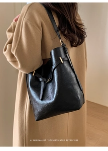 Détail du sac seau noir avec boucle dorée et large bandoulière sur un manteau en laine