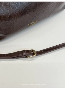 Detail of dark brown glossy leather texture with vintage pleats and gold logo accent