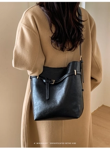 Vista posteriore della borsa a secchiello nera in pelle indossata con cappotto beige