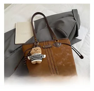 Macro shot of brown retro tote bag featuring leather handles and a cute plush bear charm