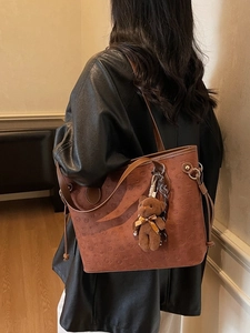 Brown tote bag with embossed teddy dog pattern and plush bear charm worn by a model