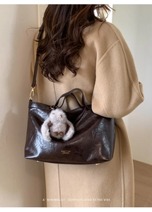 Deep brown oil-wax leather tote bag detail with logo and plush rabbit pendant