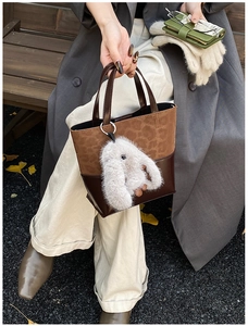 Detail of color-block tote bag with leopard texture and plush bunny charm in autumn setting