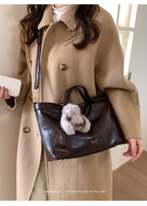 Detail of dark brown glossy leather tote bag with a cute plush rabbit charm and shoulder strap