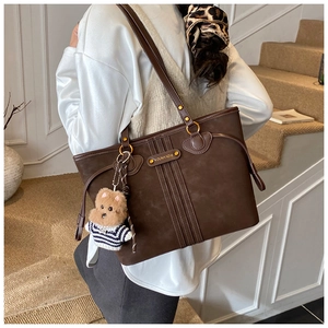 Détail d'un sac cabas marron foncé avec charm ours porté par un mannequin