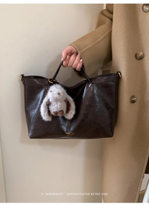Detail of vintage brown tote bag with smooth texture and soft plush bunny keychain
