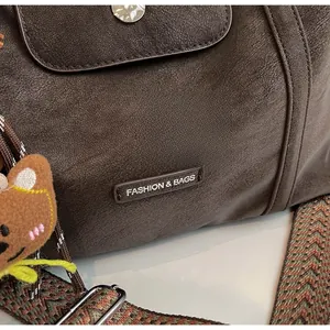 Detail of dark brown matte texture handbag with woven strap and bear charm accessory
